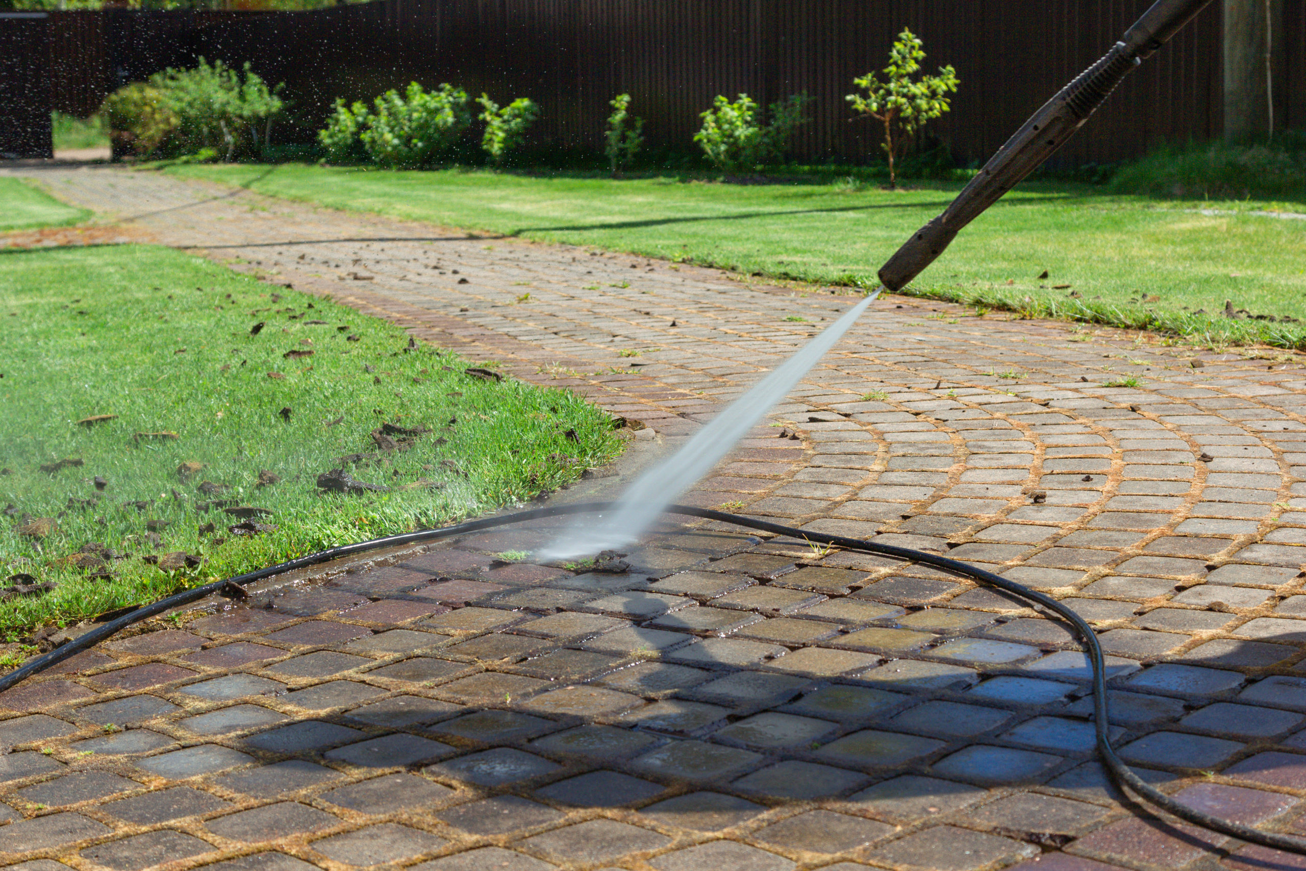 Cleaning street with high pressure power washer, washing stone garden path